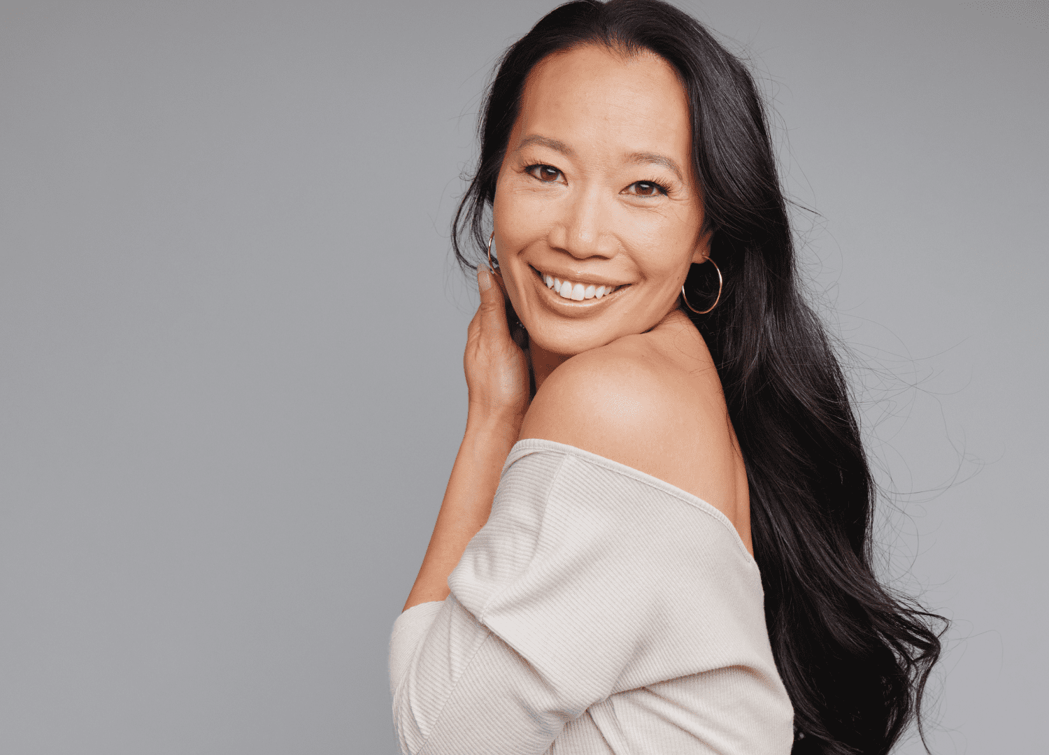 Confident woman with radiant skin and long dark hair, smiling after a facial fat transfer procedure for a youthful look.